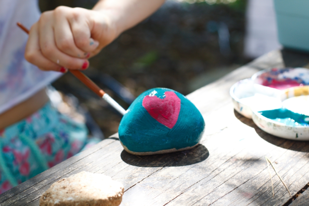 Picture of a hand painting a rock with a pink heart