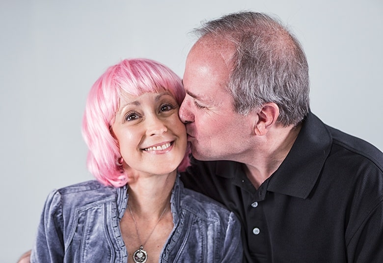 Breast cancer survivor, Vicki Johnson, modeling a pink wig, alongside her husband