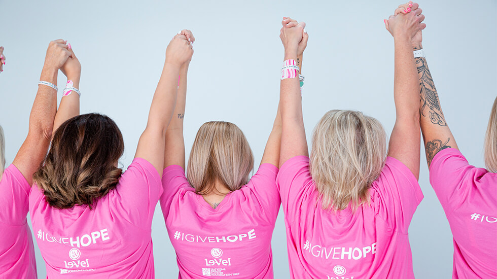 Women facing backwards holding hands in the air with bright pink shirts