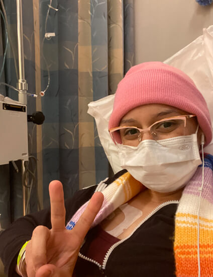 Michelle getting chemo with mask on showing the peace sign