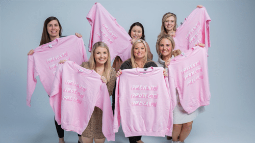 SABRE's female employees holding pink sweaters that say prevent, protect, prevail