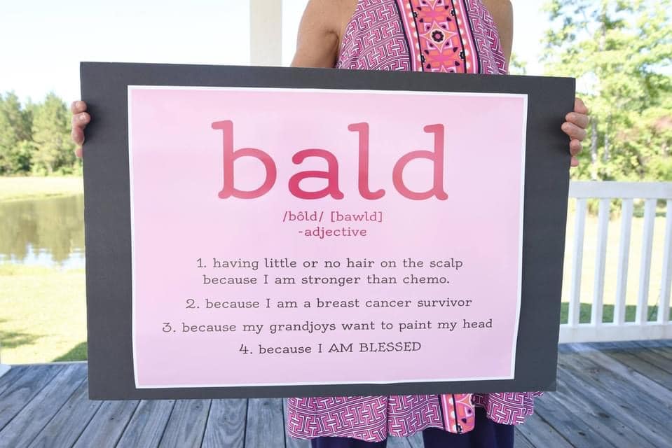 Sheri holding a poster with "bald" and alternative meanings: 1. having little her because I am stronger than chemo, a breast cancer survivor, blessed
